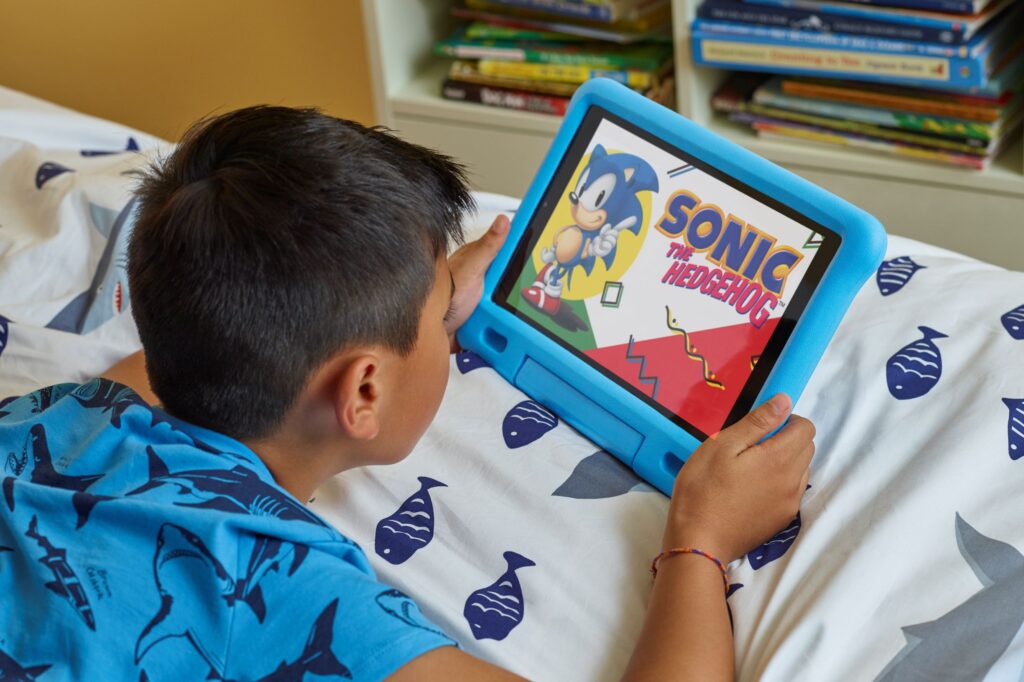 Child holding Fire HD 10 Kids Edition Tablet on bed.