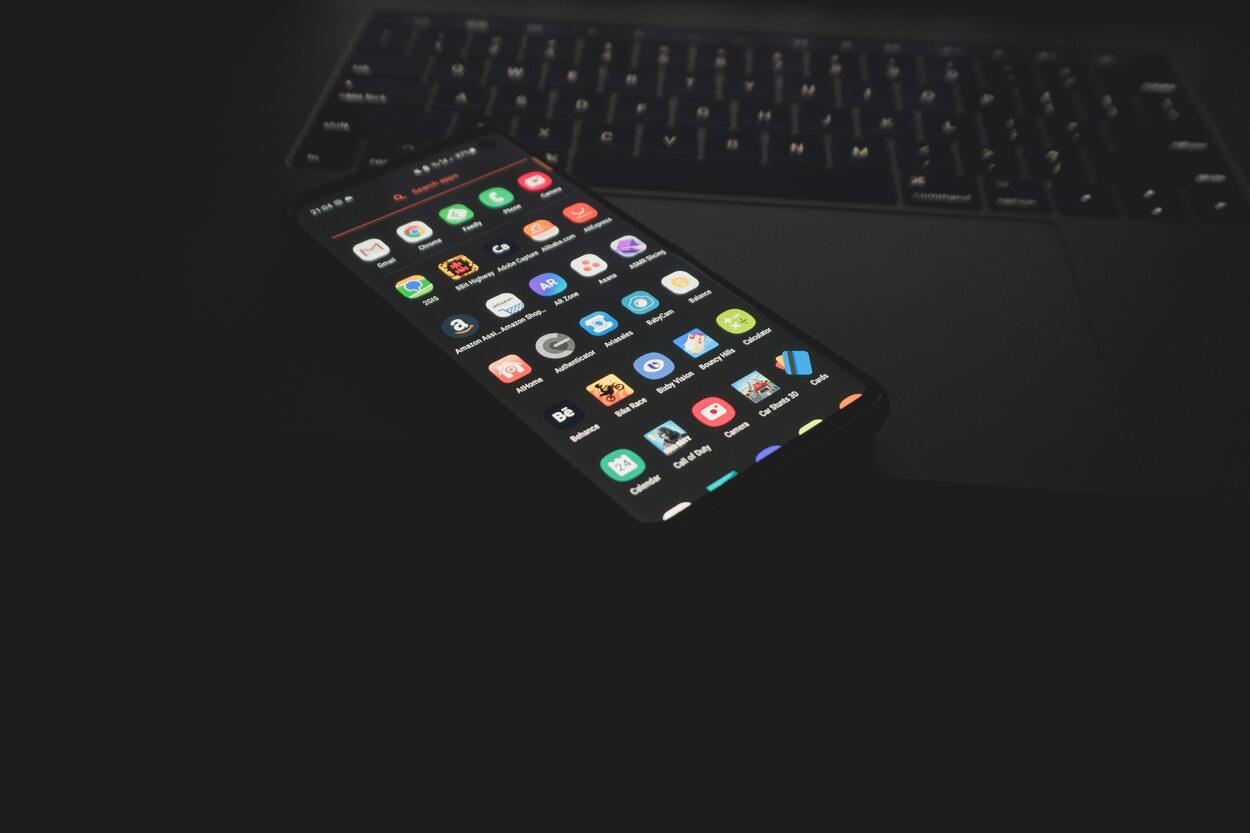 Black android phone with multiple apps on top of a black laptop.