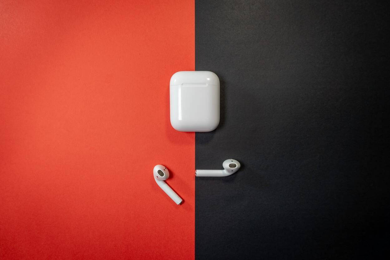 White AirPods and its charging case on a half black and half red background.