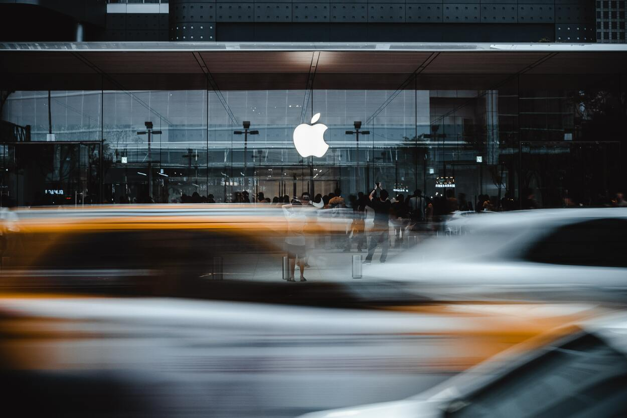 People around the Apple logo taking pictures while cars passing by.