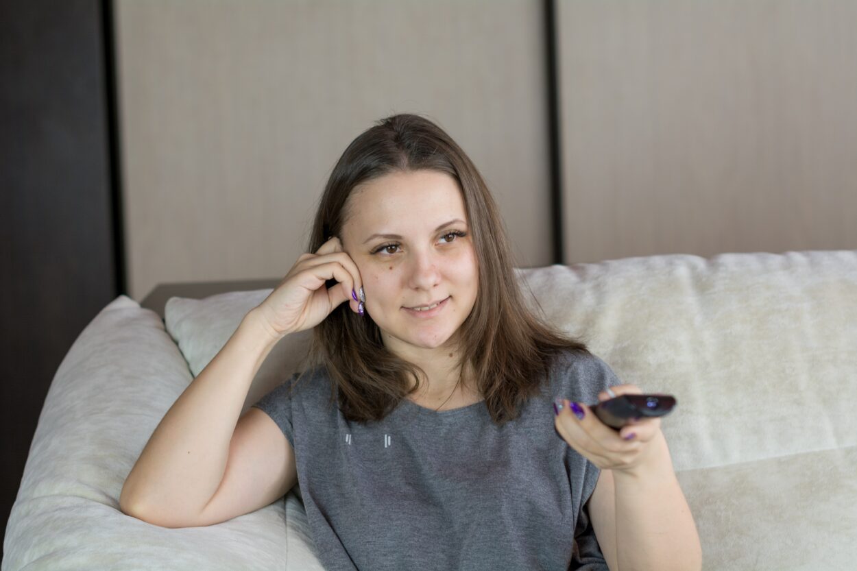 A woman sitting on a sofa and pointing the remote