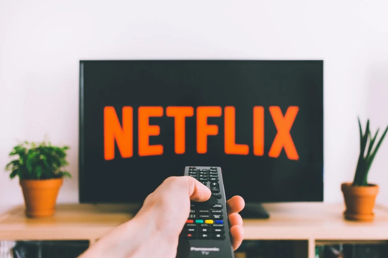 A person holding the remote and pointing towards the TV that has Netflix logo displayed