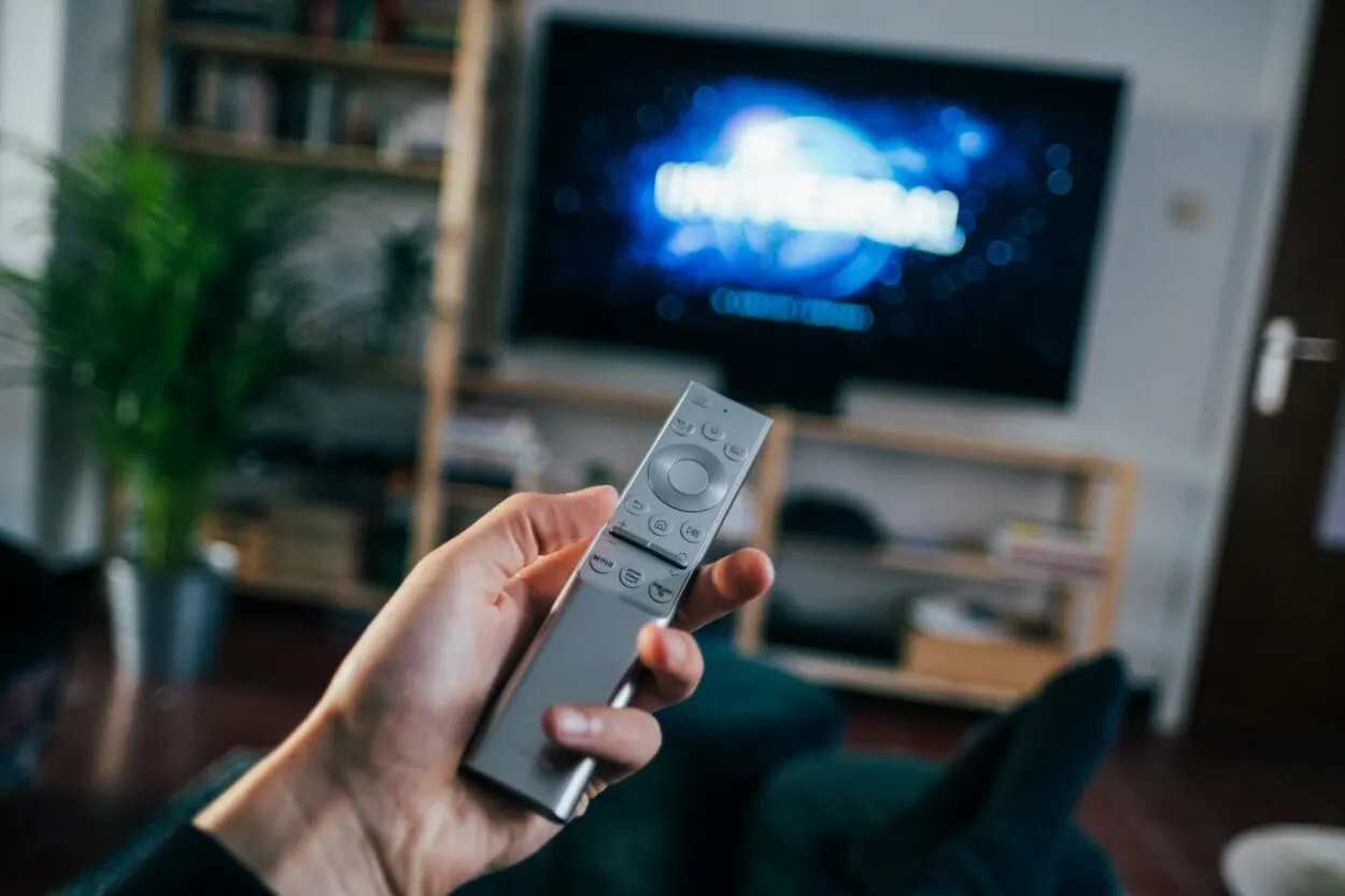 A person holding the remote with the TV on in the background