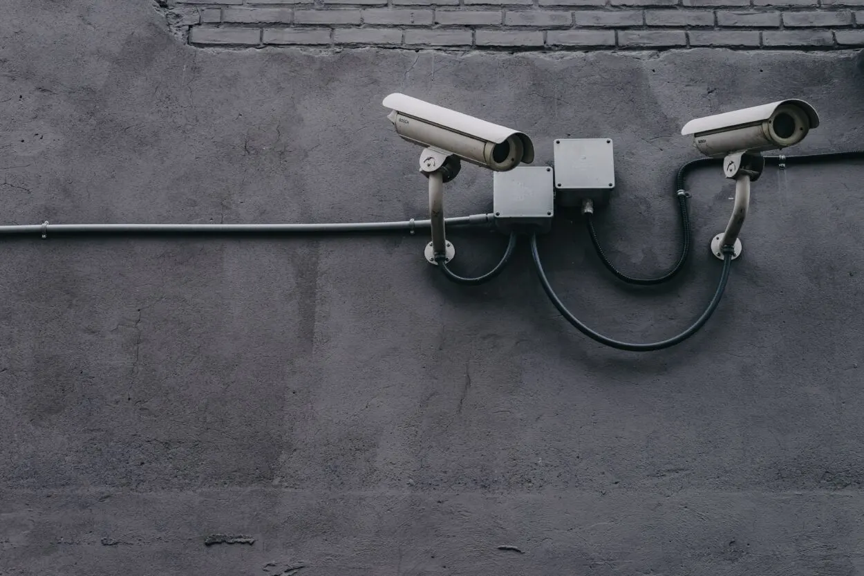 Two white colored wired CCTV camera installed on gray wall