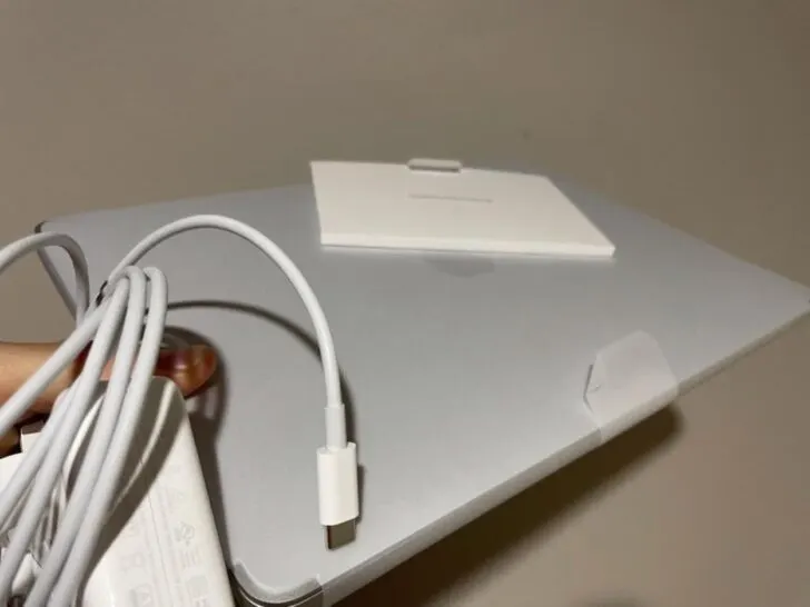 A person holding a MacBook Pro and its charger