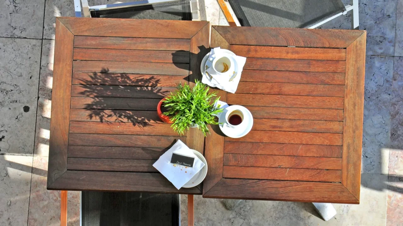 Wooden table of cafe with potted plant, coffee cups and chairs.
