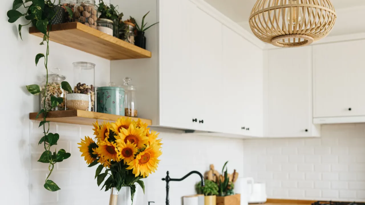 View on clean white simple modern kitchen in scandinavian style, kitchen details, wooden table, sunflowers bouquet in vase on the table