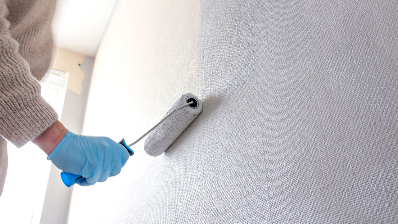 Cropped view of a man’s hands skillfully rolling paint onto a wall, ensuring a smooth and even finish.