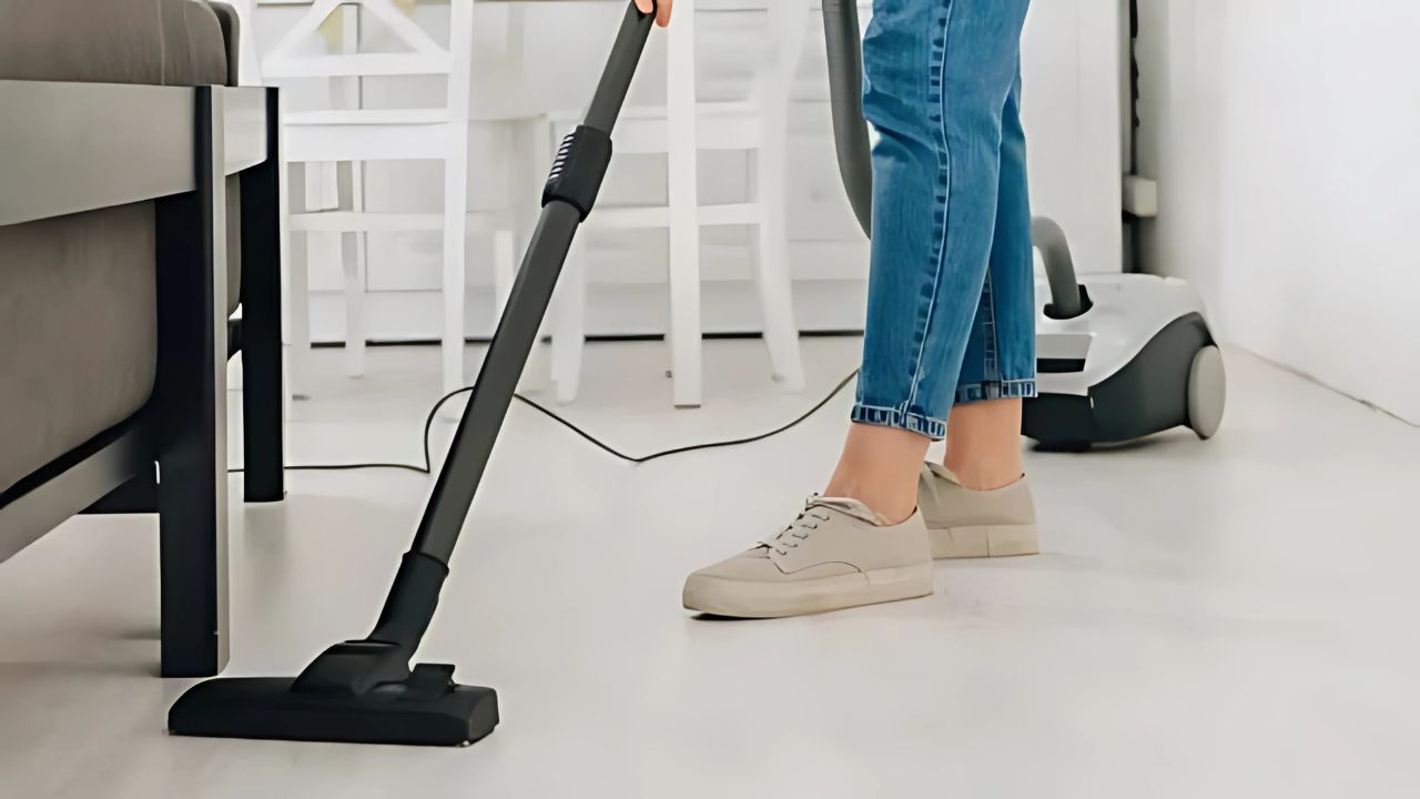 Cropped view of woman cleaning floor with vacuum cleaner.