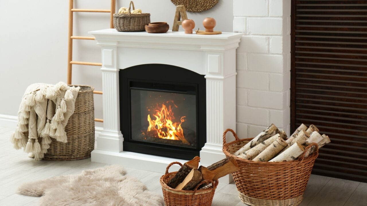 Wicker baskets with firewood, beige furry rug and white fireplace in cozy living room
