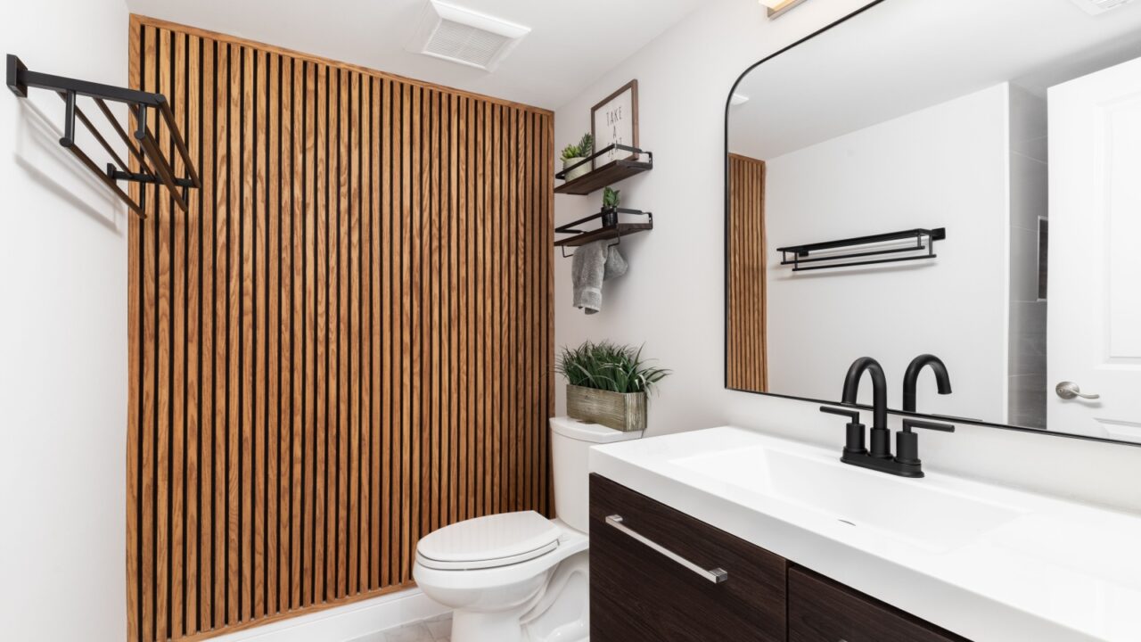 A bathroom with a dark wood cabinet, floating shelves with decorations above the toilet, and a wood slat accent wall.