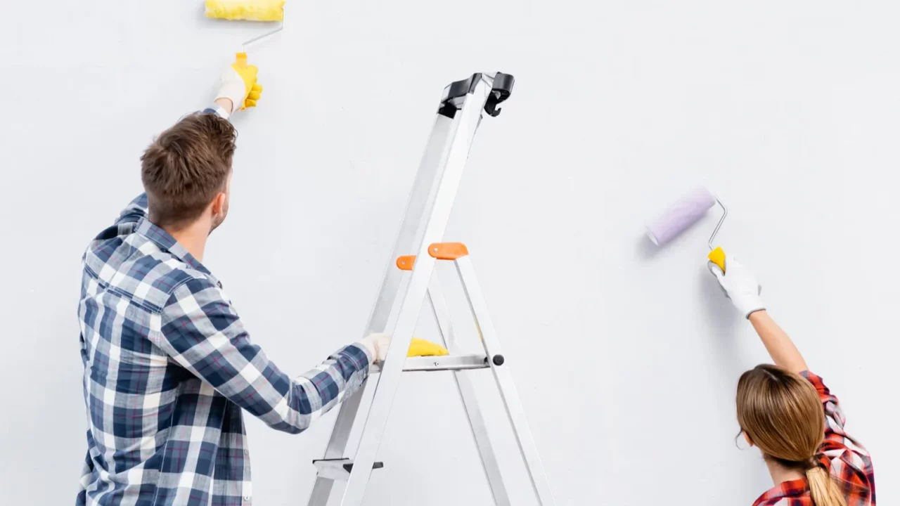 back view of young couple with rollers painting wall near